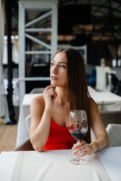 Beautiful young girl sits and drinks wine on the veranda of a beautiful house. Holiday.