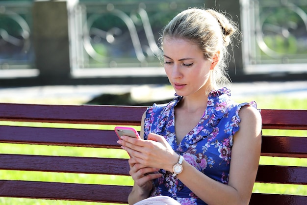 Beautiful young girl sitting on a bench and looking at mobile phone