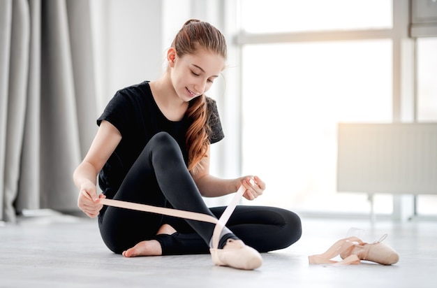 Beautiful young girl sitting on the floor and wearing pointe shoes