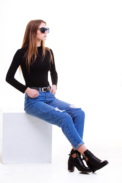 Beautiful young girl sitting on a white cube in the Studio with insulation.