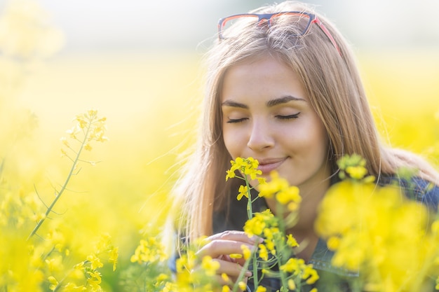 Beautiful young girl smells yellow flowers on a meadow with her eyes closed, smiling.