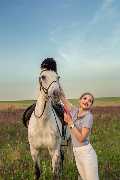 Beautiful young girl smile at her horse dressing uniform competition: outdoors portrait on sunset. Taking care of animals, love and friendship concept.