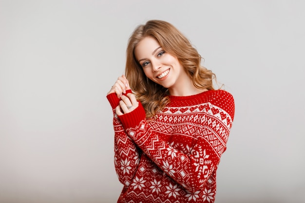 Beautiful young girl smiling in a red sweater with ornament on a gray background indoors