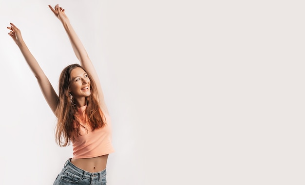 Beautiful young girl smiling and stretches her arms up and laughs looking at the camera on a white isolated background. Positive brunette woman. Kind look. Beauty face