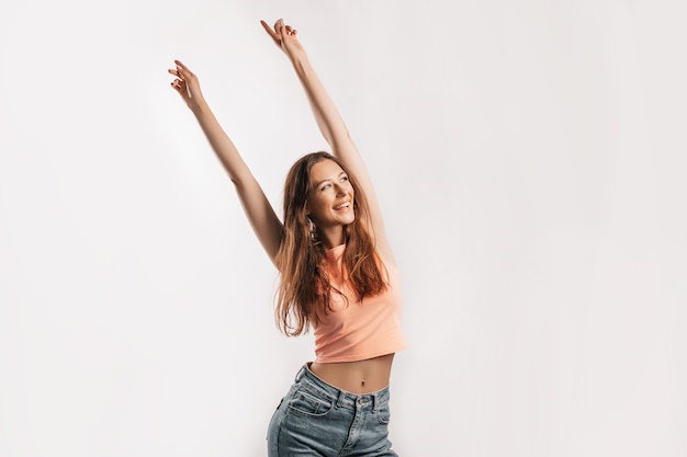 Beautiful young girl smiling and stretches her arms up and laughs looking at the camera on a white isolated background. Positive brunette woman. Kind look. Beauty face