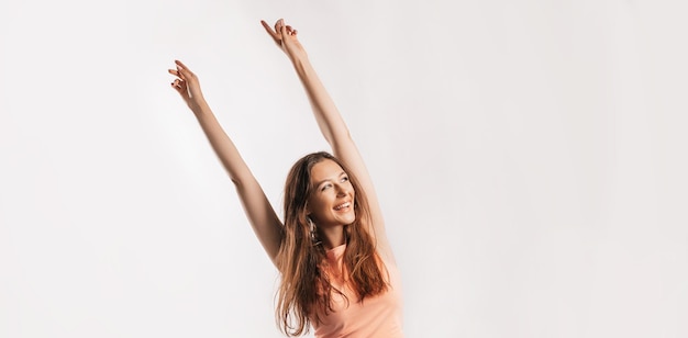 Beautiful young girl smiling and stretches her arms up and laughs looking at the camera on a white isolated background. Positive brunette woman. Kind look. Beauty face