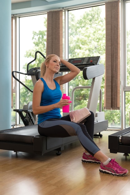 Beautiful Young Girl Sportswoman Sitting on Treadmill and Resting After Training in Gym or Fitness Club