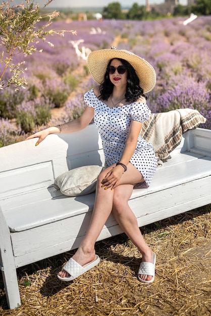 Bella ragazza in un cappello di paglia seduto su uno sfondo di campo di lavanda