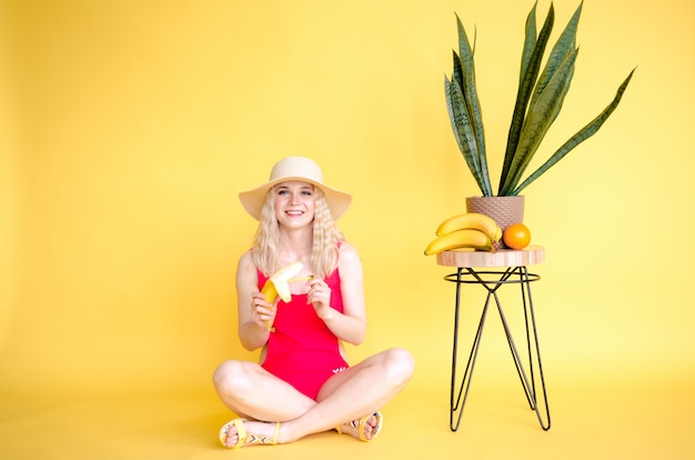 A beautiful young girl in straw hat sitting near a yellow background