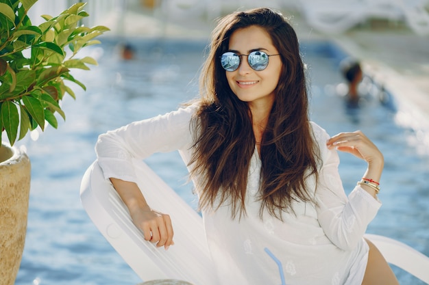 A beautiful young girl in a straw hat sitting on a summer terrace by the pool 