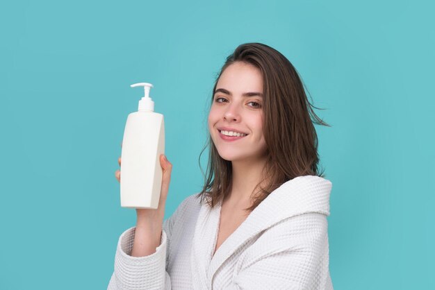 A beautiful young girl in the studio with wet hair. Beauty haircare cosmetics. Woman hold bottle shampoo and conditioner. Balm bottle.