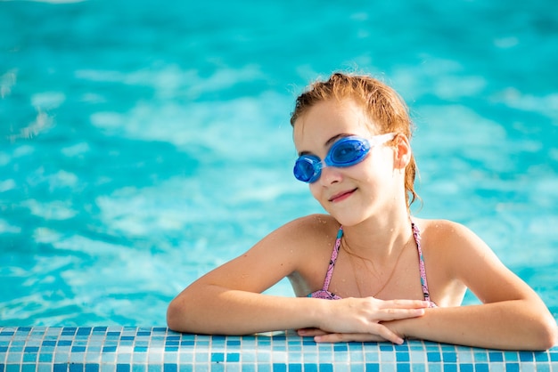 A beautiful young girl in a swimsuit bathes in a pool with blue clear water in blue swimming glasses. Summer. Rest. Vacation.