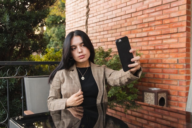 Beautiful young girl taking a selfie with her smartphone in an outdoor cafe