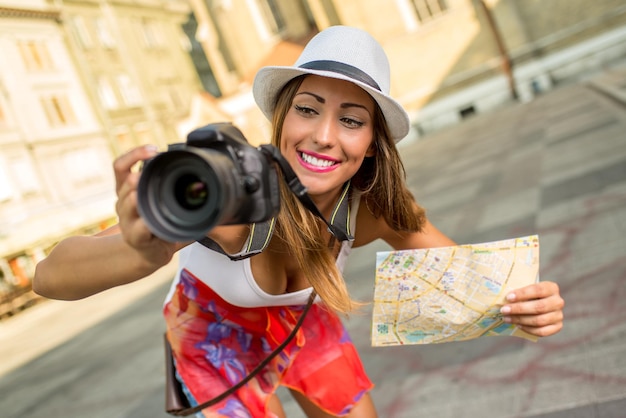 Beautiful young girl tourist holding map and photographing with digital camera.