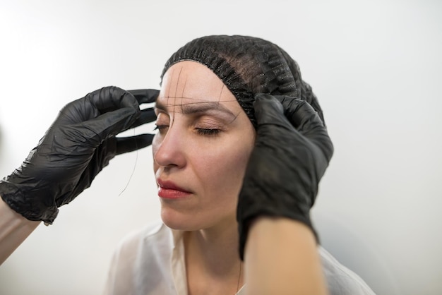 beautiful young girl tweezing her brows in a beauty salon beauty concept cosmetologist plucks client eyebrows by thread eyebrow correction threading permanent makeup microblading brow close up