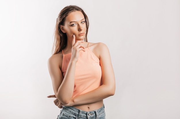 Beautiful young girl unhappy frown and thinks on gray isolated background. Serious woman looks to the side and holds hand to face