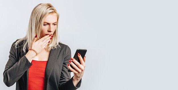 Beautiful young girl unhappy and holding phone on gray isolated surface