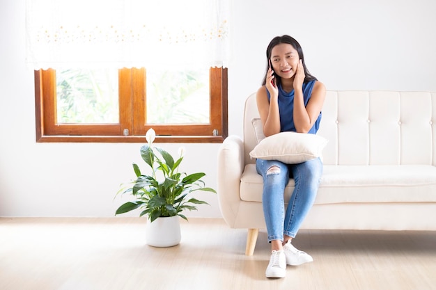 Beautiful young girl use smartphone sitting on sofa at home