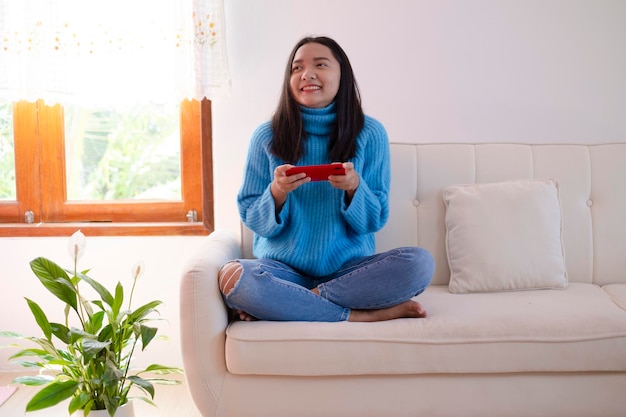 Beautiful young girl use smartphone sitting on sofa at home