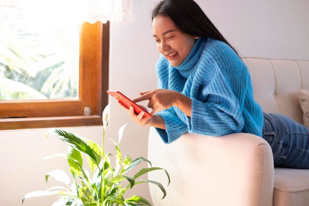 Beautiful young girl use smartphone sitting on sofa at home