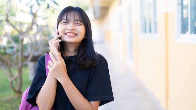 学校でスマートフォンを使用している美しい少女アジアの女の子オレンジ色の背景