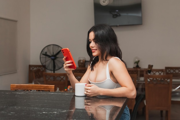 부엌에서 커피 한 잔을 마시면서 휴대전화를 사용하는 아름다운 소녀
