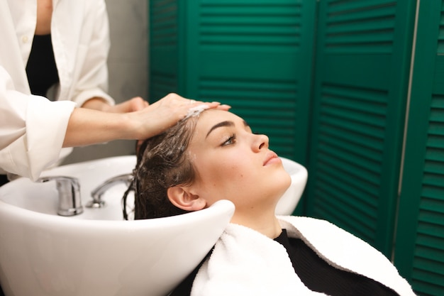 Beautiful young girl washes her head in a beauty. Hairdresser is washing hair for client