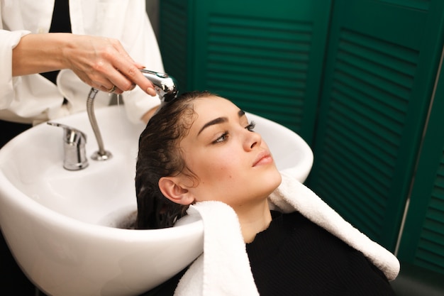 Beautiful young girl washes her head in a beauty. Hairdresser is washing hair for client