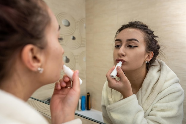 Beautiful young girl in a white coat makes a boring makeup to a spacious mirror. The concept of makeup itself