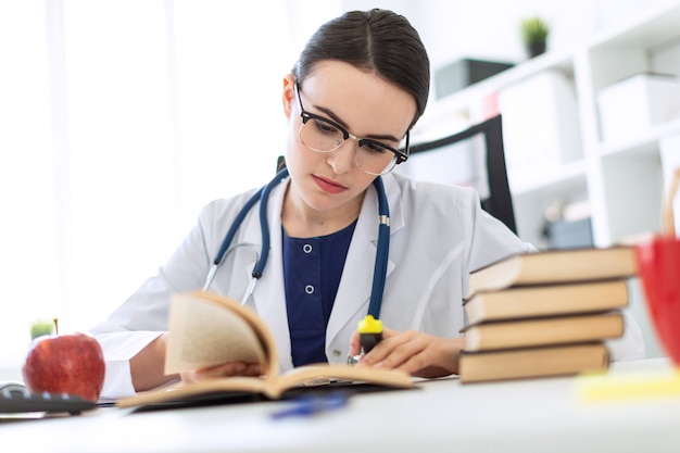 Una bella ragazza vestita di bianco è seduta alla scrivania del computer con un pennarello e un libro. una fotografia con una profondità di nitidezza, un focus evidenziato sulla ragazza.