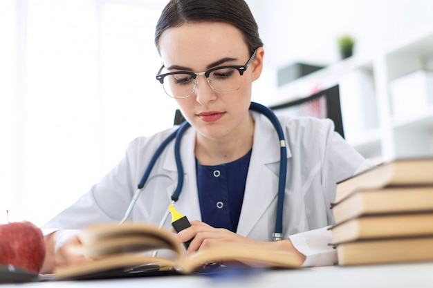 A beautiful young girl in a white robe is sitting at the computer desk with a marker and a book.