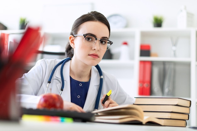 A beautiful young girl in a white robe is sitting at the computer desk with a marker and a book. 