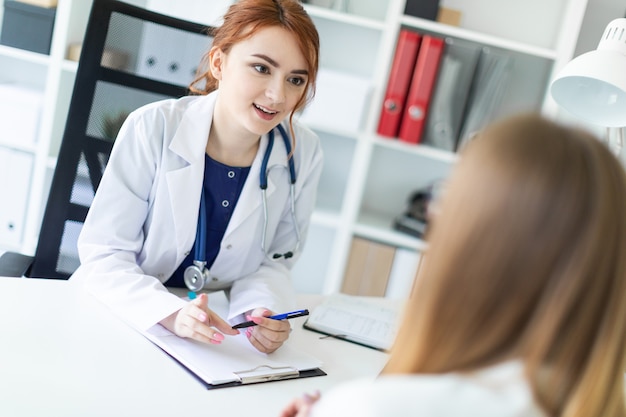 A beautiful young girl in a white robe is sitting at the desk in the office and communicating with the interlocutor. 