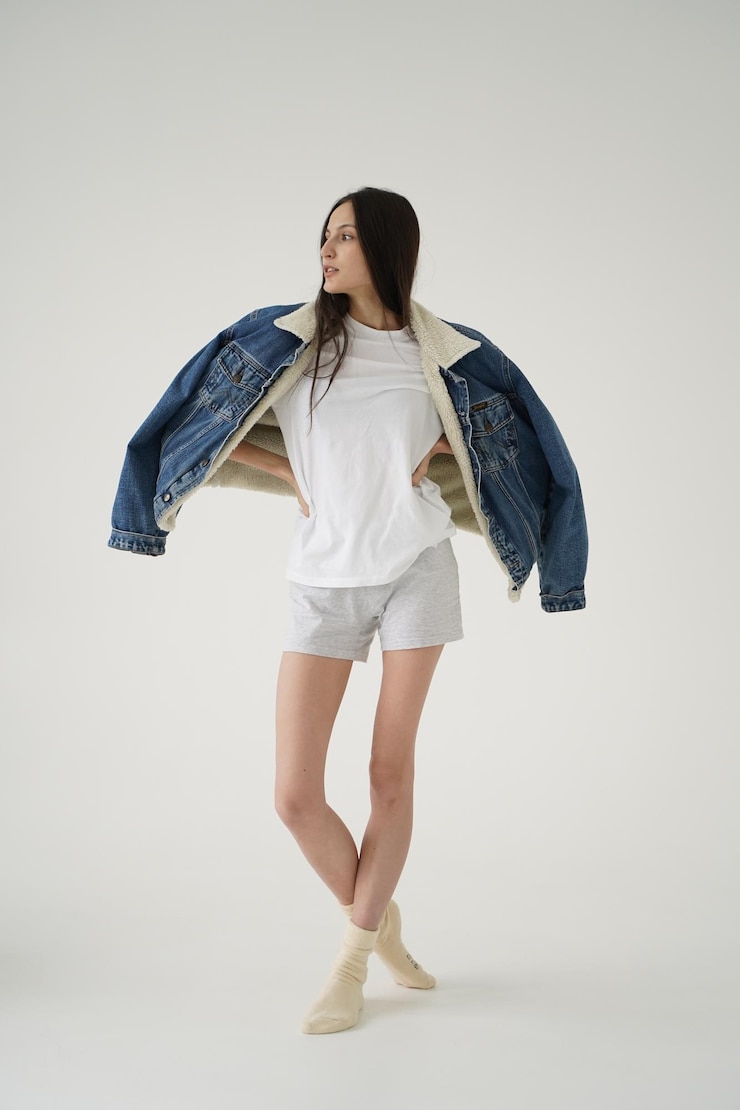 Photo 白いtシャツ ⁇ 短い白いショートパンツ ⁇ 白い背景の暖かいデニムジャケットを着た美しい若い女の子 ⁇ 