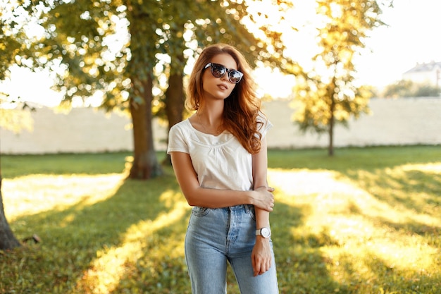 Beautiful young girl in a white Tshirt and vintage jeans with sunglasses in the park on a sunny day