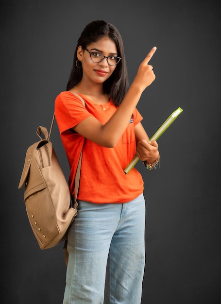 Beautiful young girl with a backpack standing and holding a notebook posing on a grey background