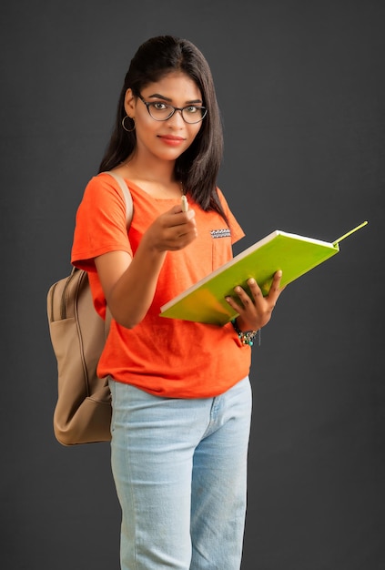 Beautiful young girl with a backpack standing and holding a notebook posing on a grey background