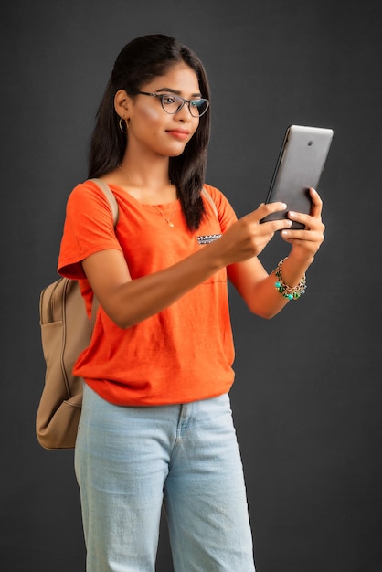 Beautiful young girl with a backpack using mobile phone or smartphone on gray background