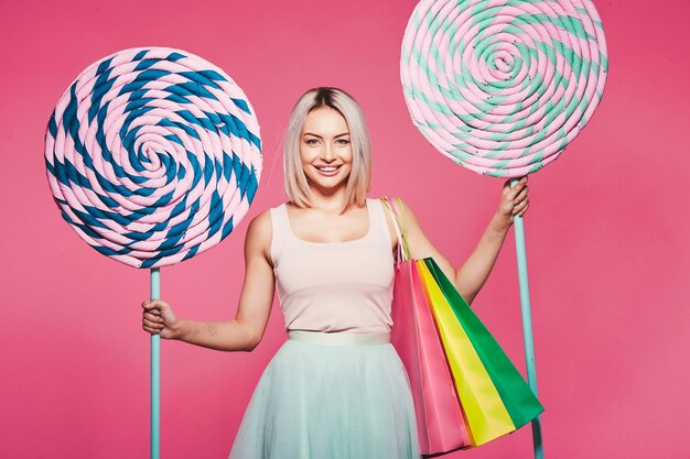 Beautiful young girl with blonde hair wearing top and skirt standing with huge sweet lollypops