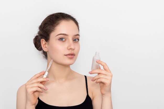 Beautiful young girl with bottle and a pipette of collagen serum in her hands