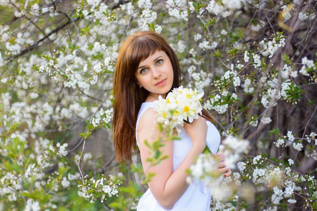 Beautiful young girl with a bouquet of daffodils in a white dress