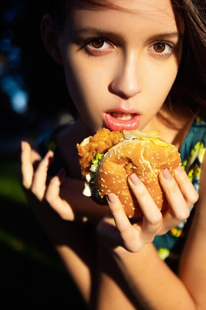 自然の中でハンバーガーを持つ美しい少女。