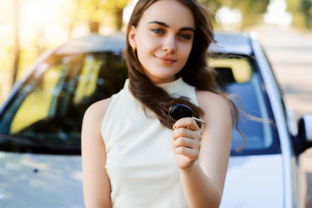 車のキーを手にした美しい少女が新しい車の近くに立って、購入を自慢している