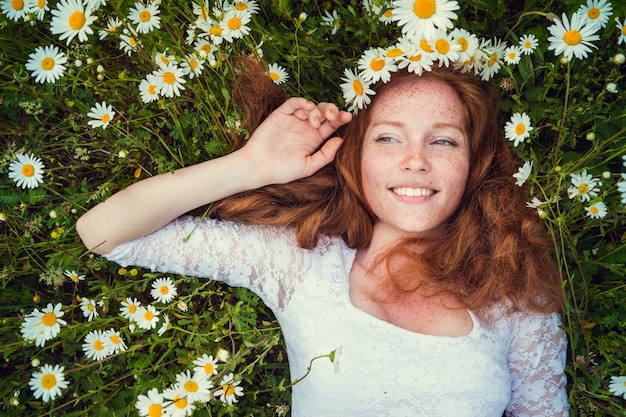 Foto bella ragazza con capelli rossi ricci nel campo della camomilla