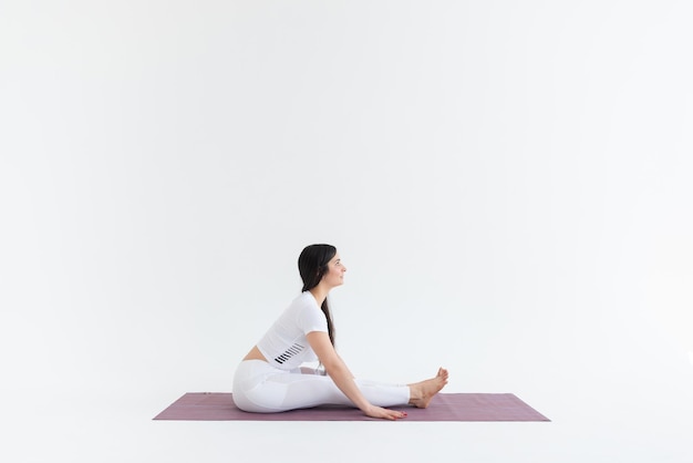 a beautiful young girl with dark hair stands in the Paschimottanasana pose on a white background