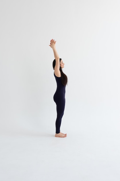 a beautiful young girl with dark hair stands in the Urdhva Hastasana pose on a white background