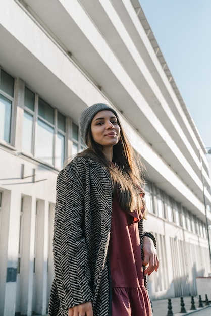 Bella e giovane ragazza con capelli lunghi scuri in un cappello grigio cappotto e vestito bordeaux ritratto di uno smi