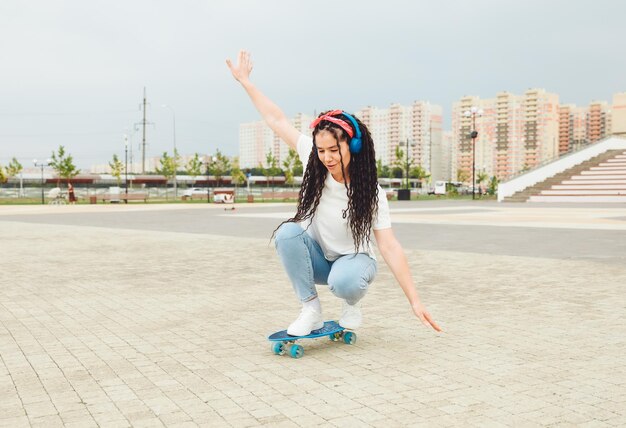 ドレッドヘアを持つ美しい少女が、晴天のジェネレーション z でスケート ボードに乗る