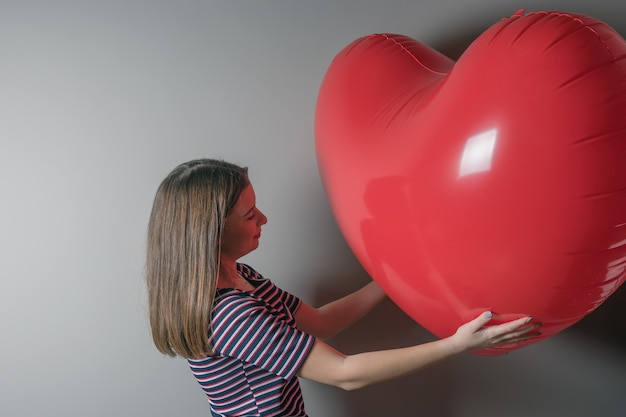 Beautiful young girl with heart shape balloon on bright background