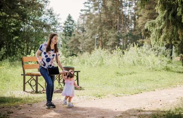 beautiful and young girl with her little girl for a walk playing in a park outdoors near a forest